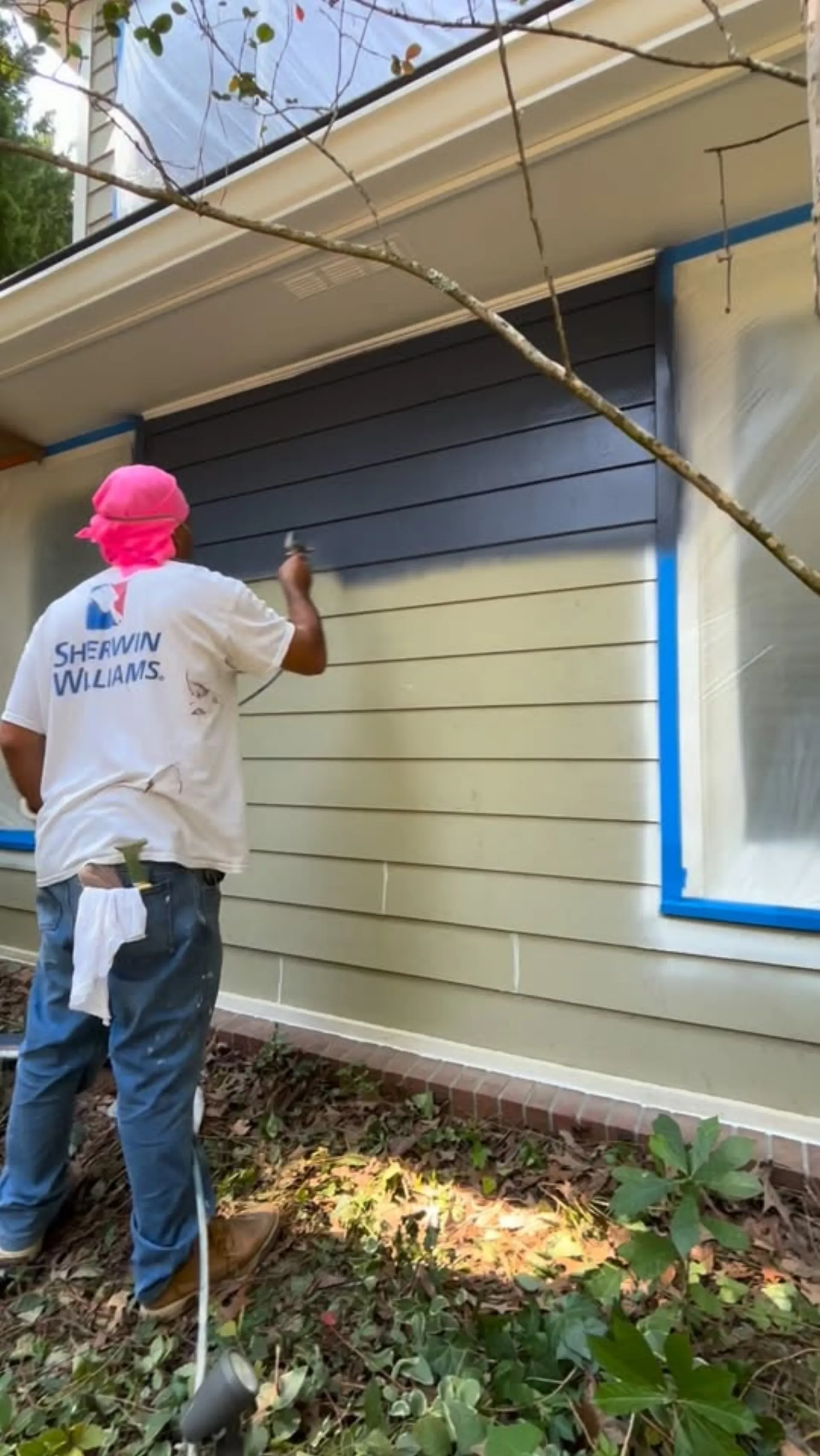 Painter brushing exterior siding beside a masked window